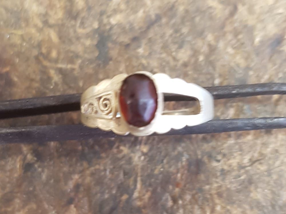 Antieke gouden ring met een donkerrode granaat; het rechterschoudertje mist zijn opengewerkte krullen
